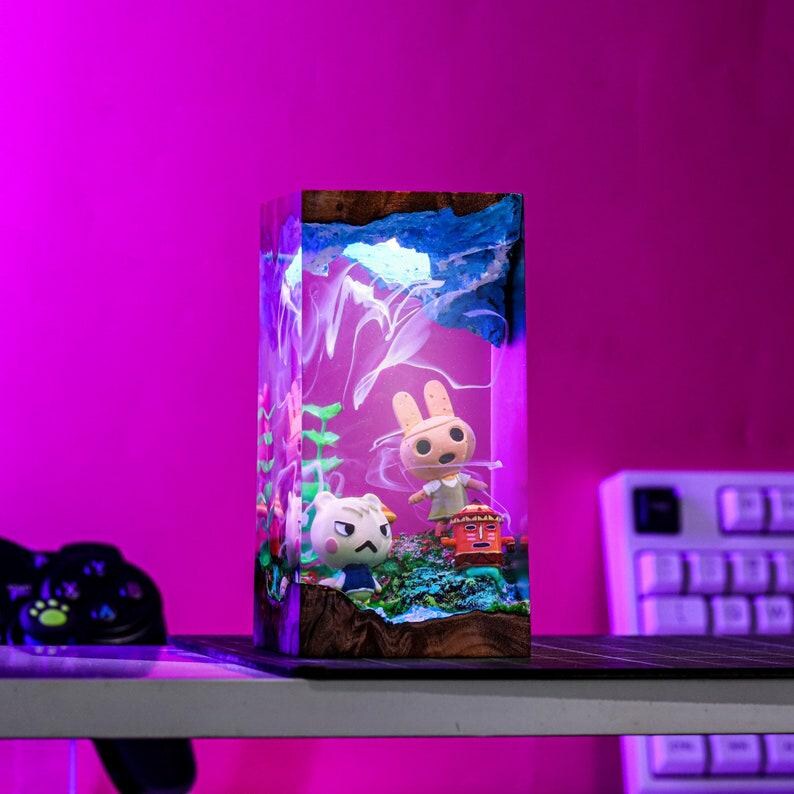 May include: A rectangular resin art piece featuring miniature figurines of cartoon characters. The artwork has a vibrant, colorful design with a purple and blue background. The figurines are set in a landscape with plants and a wooden base.