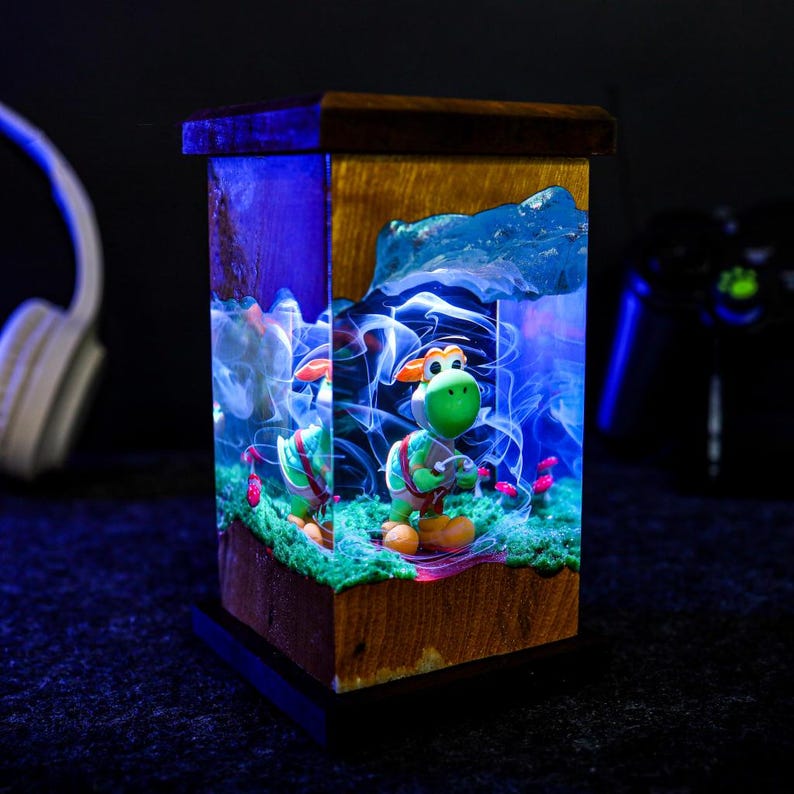 May include: A wooden and resin lamp featuring a green cartoon character. The lamp has a rectangular shape with a wooden frame and a resin interior. The interior is illuminated with blue and white lights, creating a vibrant and colorful display.