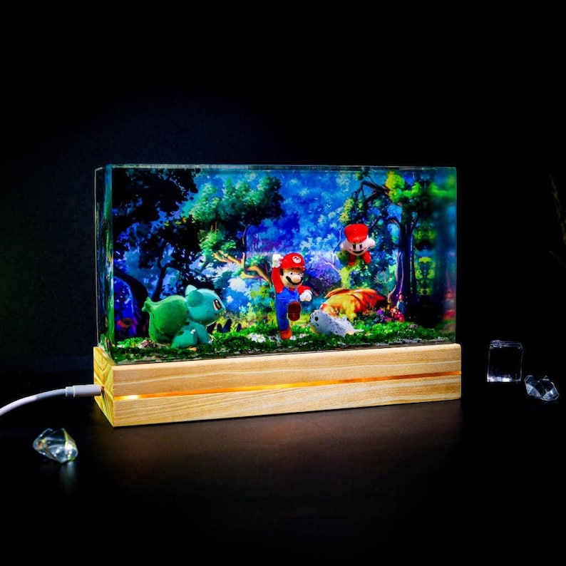 Puede incluir: Diorama rectangular de resina con Mario, Luigi y Bulbasaur en una escena de bosque. El diorama est&aacute; iluminado por una luz c&aacute;lida desde una base de madera. El fondo representa un bosque vibrante y colorido.