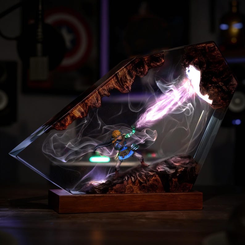 May include: A decorative resin sculpture featuring a miniature figure wielding a glowing energy beam. The sculpture is encased in clear resin with wood accents and sits on a wooden base. The figure is dressed in blue and gold.