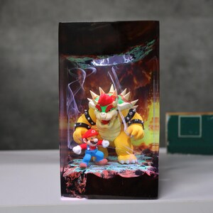 Op de afbeelding: Een rechthoekige display met de personages Bowser en Mario uit de Super Mario-videogameserie. Bowser, een groot geel schildpadachtig wezen met een rode hanenkam, staat dreigend naast het kleinere Mario-figuur. De achtergrond toont een vurige sc&egrave;ne.