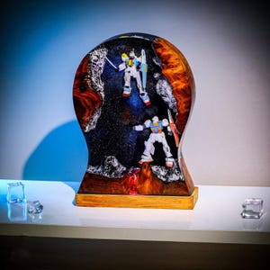 May include: A wooden sculpture featuring two robot figures set against a starry background. The sculpture has a dark, textured interior and a warm, amber-colored exterior. The base is a light brown.