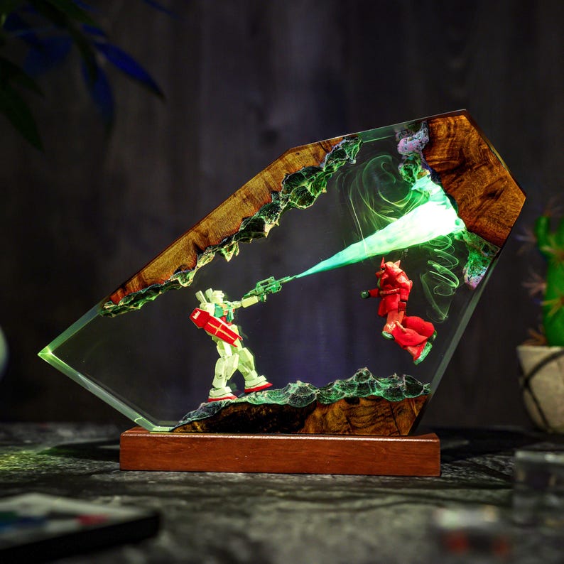 Puede incluir: Una pieza de arte en resina &uacute;nica que presenta dos figuras de robots en una escena de batalla. La obra de arte est&aacute; encerrada en resina transparente con una base y detalles de madera. Las figuras son verdes y rojas, con un efecto de rayo l&aacute;ser verde.