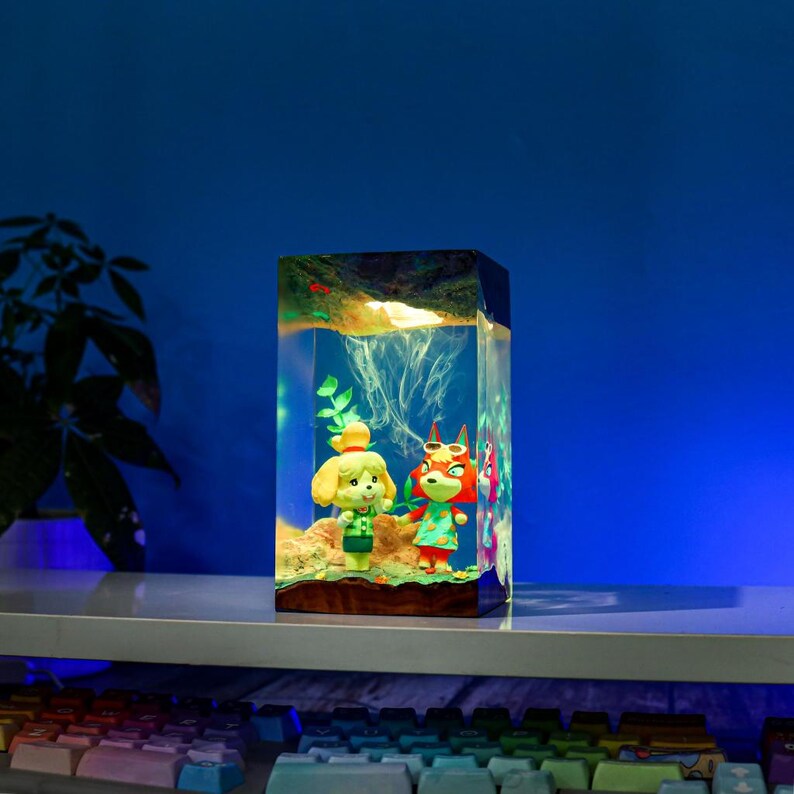 May include: A rectangular resin art piece featuring two cartoon characters in a miniature underwater scene. The figures are set against a backdrop of simulated coral and aquatic plants, with a wooden base and a glowing effect.