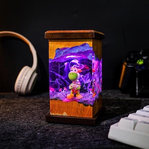 May include: A wooden lamp with a Yoshi figurine inside, illuminated by purple and pink lights. The lamp has a rectangular shape with a dark brown base and top. The Yoshi figure is green, white, and orange.