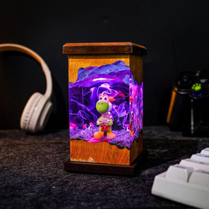 May include: A wooden lamp with a Yoshi figurine inside, illuminated by purple and pink lights. The lamp has a rectangular shape with a dark brown base and top. The Yoshi figure is green, white, and orange.