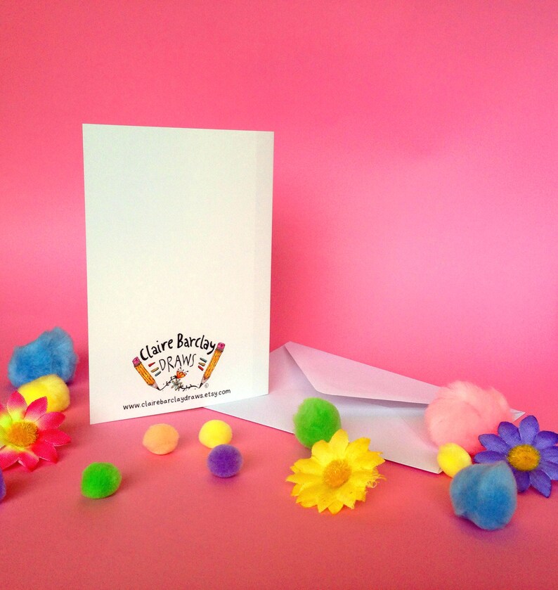 May include: A white card with a pink background. The card has the text "Claire Barclay Draws" and a website address. The card is surrounded by colorful pom-poms and flowers.