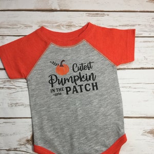 May include: A gray and orange baby onesie with the text "Cutest Pumpkin in the Patch" and a small pumpkin graphic.