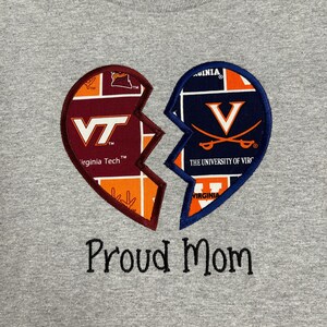 May include: A gray t-shirt featuring a broken heart design. One half displays the Virginia Tech logo in maroon, orange, and white. The other half shows the University of Virginia logo in navy and orange. The text "Proud Mom" is embroidered below.