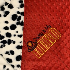 May include: A red and white baby blanket with a dalmatian print on one side and a red side with the text "Daddy is my HERO" embroidered in yellow with a firefighter helmet graphic.