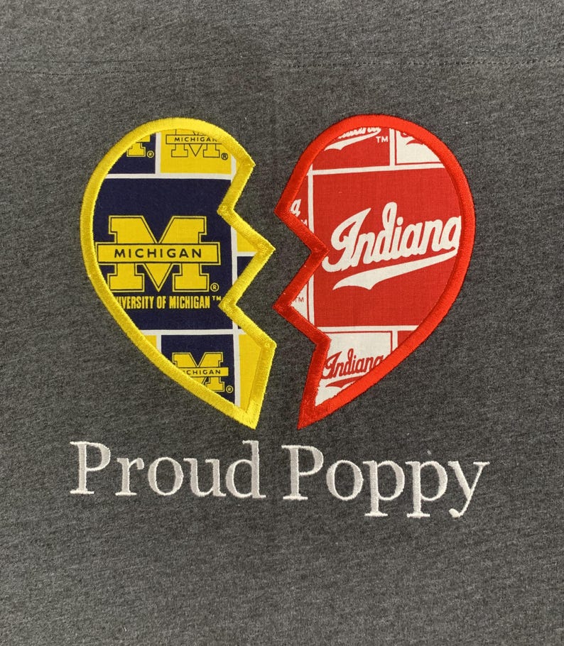 May include: Gray sweatshirt featuring a broken heart design. One half is yellow and navy blue with "Michigan" text, the other is red with "Indiana" text. The words "Proud Poppy" are embroidered below.