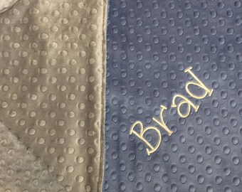 May include: A gray and blue baby blanket with a soft, textured surface. The blanket is personalized with the name "Brad" embroidered in gold thread.