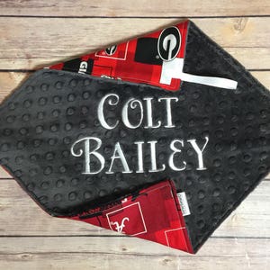 May include: A gray and red baby blanket with a gray minky backing. The blanket is personalized with the name "Colt Bailey" in white embroidery.