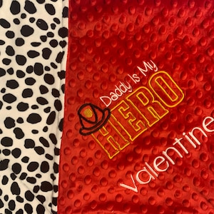 May include: Red and white minky baby blanket with a black and white dalmatian print on one side. The other side has an embroidered design that says "Daddy is my HERO Valentine" with a firefighter helmet graphic.