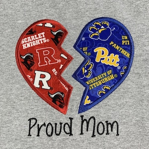 May include: A gray t-shirt with a broken heart design. The left side of the heart is red and features the Rutgers Scarlet Knights logo and the letter "R". The right side of the heart is blue and features the University of Pittsburgh Panthers logo and the word "Pitt". The text "Proud Mom" is embroidered below the heart.