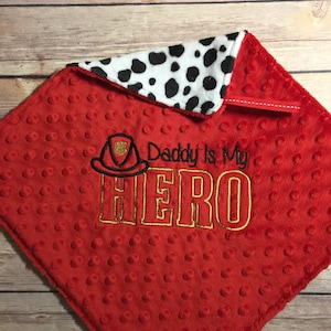 May include: Red and white baby blanket with a black and white dalmatian print on one side. The other side has a red background with white polka dots and an embroidered firefighter helmet with the text "Daddy is my HERO".
