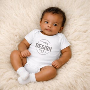 Puede incluir: Un body de beb&eacute; blanco de manga corta con el texto YOUR DESIGN HERE en un gr&aacute;fico circular en el pecho. La prenda tiene cuello redondo y cierres a presi&oacute;n en la parte inferior, y se lleva con calcetines blancos a juego.