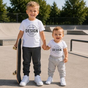 Puede incluir: Una camiseta blanca de manga corta y un body blanco de manga corta, ambos con un gr&aacute;fico circular con el texto YOUR DESIGN HERE. La camiseta se combina con pantalones de ch&aacute;ndal gris oscuro y el body con pantalones de ch&aacute;ndal de color gris claro.