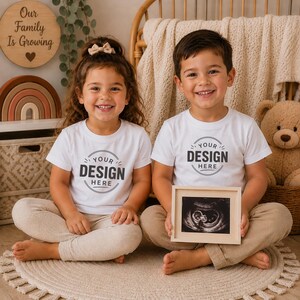 Puede incluir: Dos ni&ntilde;os con camisetas blancas de manga corta con el texto "YOUR DESIGN HERE" impreso en un gr&aacute;fico circular en el pecho. Un ni&ntilde;o sostiene un peque&ntilde;o marco de madera clara que contiene una imagen de ecograf&iacute;a en blanco y negro.