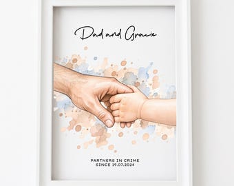 May include: A framed print featuring a watercolor illustration of an adult hand holding a small child's hand. The text reads "Dad and Gracie" at the top and "PARTNERS IN CRIME SINCE 19.07.2024" at the bottom, set against blue and tan paint splatters.