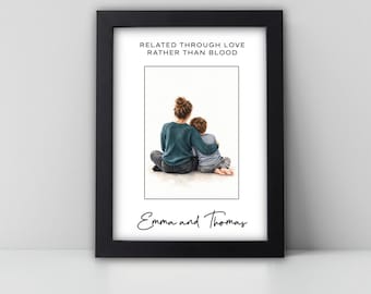 May include: A black framed print featuring a watercolor illustration of an adult and a child sitting together. The text reads "RELATED THROUGH LOVE RATHER THAN BLOOD" at the top and "Emma and Thomas" in script at the bottom.