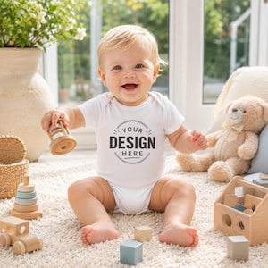 Puede incluir: Un body blanco de manga corta para beb&eacute; con un gr&aacute;fico circular en el pecho que incluye el texto YOUR DESIGN HERE. La prenda la lleva un beb&eacute; sentado sobre una alfombra texturizada, rodeado de varios juguetes de madera y un oso de peluche.