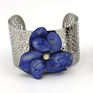 May include: Three silver metal bracelets with a cutout design. Each bracelet features a different colored enamel flower, one blue, one purple, and one dark blue.