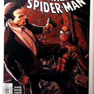 May include: Comic book cover for "The Amazing Spider-Man" featuring Spider-Man in a red and black suit being confronted by a man in a suit holding a gun. The title "The Chameleon Conspiracy" is at the top.