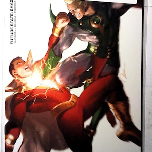Könnte beinhalten: Comic-Cover für Future State: Shazam! #2. Das Cover zeigt zwei Figuren in einer Kampfszene, eine in Rot und Gold, die andere in Grün und Schwarz. Der Comic befindet sich in einer Schutzhülle mit einem Aufkleber von Midtown Comics.