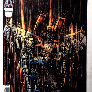 Puede incluir: Portada de cómic con una ilustración detallada de un robot Transformer en tonos naranja, amarillo y azul sobre un fondo negro. El título "TRANSFORMERS" está en letras amarillas grandes. El arte de la portada tiene un estilo dinámico y orientado a la acción.