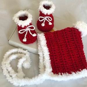May include: Red and white crocheted baby hat and booties set. The hat has a white pom-pom on top and a white trim. The booties have white trim and white bows.