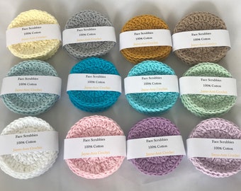 May include: Twelve crocheted face scrubbies in various colors, including yellow, gray, mustard, brown, light blue, turquoise, green, white, pink, and purple. Each scrubbie has a label that reads "Face Scrubbies 100% Cotton Jayne-Ann Crochet".