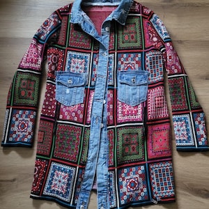 Può includere: Giacca a maniche lunghe con un design patchwork nei toni del rosa, verde e blu. Ha un colletto in denim, due tasche frontali e un pannello in denim con chiusura a bottoni. La giacca è appoggiata su una superficie di legno. Il design è fatto di quadrati.