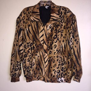 Op de afbeelding: Een vintage jasje met een opvallende dierenprint met een mix van luipaardvlekken en tijgerstrepen in bruin, beige en zwart. De jas heeft een ritssluiting, een kraag en elastische manchetten en zoom. De jas hangt aan een hanger.