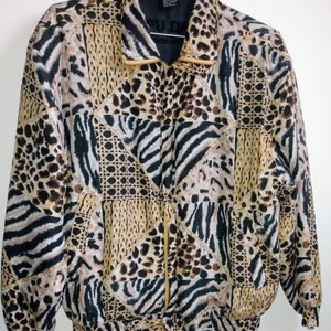 Op de afbeelding: Een vintage jas met ritssluiting en een patchwork-ontwerp met dierenprints zoals luipaard en zebra. De jas heeft een gouden rits en een zwarte kraag. Het kleurenpalet omvat bruin-, zwart- en beigetinten.