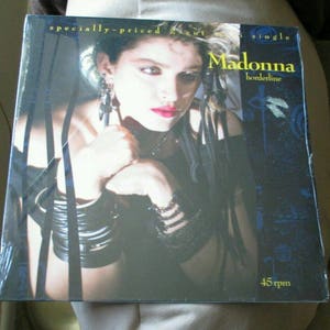 May include: A vinyl record of Madonna's single "Borderline" is shown. The album cover features a portrait of Madonna with dark hair, red lipstick, and multiple bracelets. The text "Madonna borderline" is displayed in yellow, with "45 rpm" at the bottom.