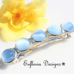 May include: A silver hair clip with five light blue round stones. The stones are set in a row on the clip. The clip is on a white background.