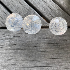 May include: Three clear, faceted, circular knobs with a multi-faceted surface design that reflects light. Each knob features a central circular indentation and a geometric, crystalline pattern across the top surface, creating a textured appearance.
