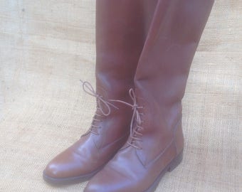 May include: A pair of brown leather riding boots with laces up the front. The boots have a pointed toe and a low heel.