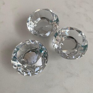 May include: Three clear, faceted glass knobs with a circular, diamond-like cut design. Each knob features a reflective, multi-faceted surface that catches light, creating a brilliant, sparkling appearance with a flat, circular center.