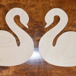May include: Two wooden swan shapes with a heart cut out of the body of each swan.