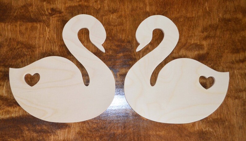 May include: Two wooden swan shapes with a heart cut out of the body of each swan.
