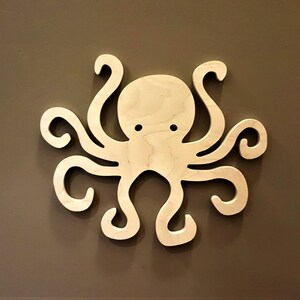 May include: A wooden cutout of an octopus with eight tentacles. The octopus is light brown and has a simple design.