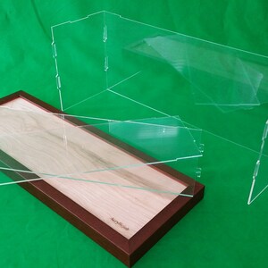 Op de afbeelding: Een rechthoekige houten vitrine met een transparant acryldeksel. De vitrine heeft een lichte houtkleur en een donkerbruine lijst. Het deksel bestaat uit twee scharnierende acryldelen.