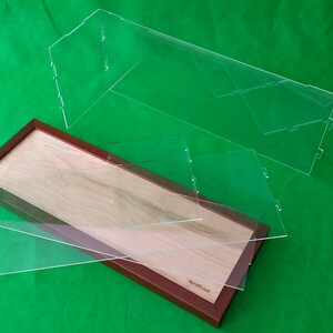 Op de afbeelding: Een houten displaykast met een transparant acryldeksel. De kast is gemaakt van licht hout met een donkerbruine lijst. De kast is leeg en klaar om items te tonen.