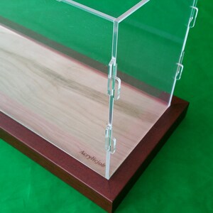 Op de afbeelding: Een transparante acryl vitrine met een houten basis. De basis is van een rijke mahonie kleur en de vitrine is gemaakt van helder acryl. De vitrine heeft een scharnierend deksel en is perfect voor het tentoonstellen van verzamelobjecten.