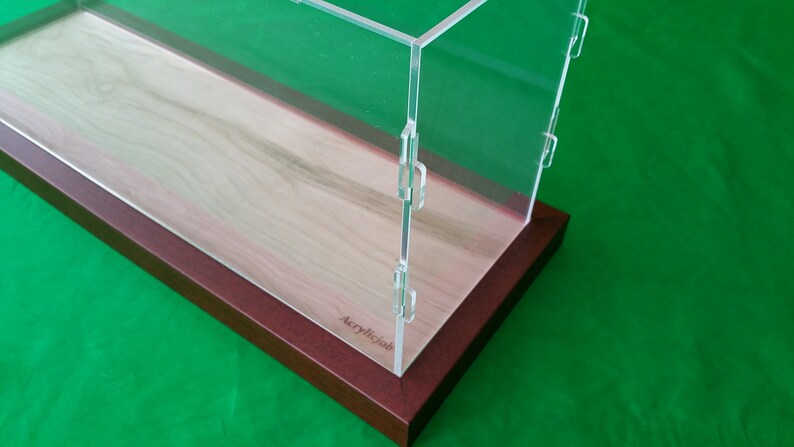Op de afbeelding: Een transparante acryl vitrine met een houten basis. De basis is van een rijke mahonie kleur en de vitrine is gemaakt van helder acryl. De vitrine heeft een scharnierend deksel en is perfect voor het tentoonstellen van verzamelobjecten.