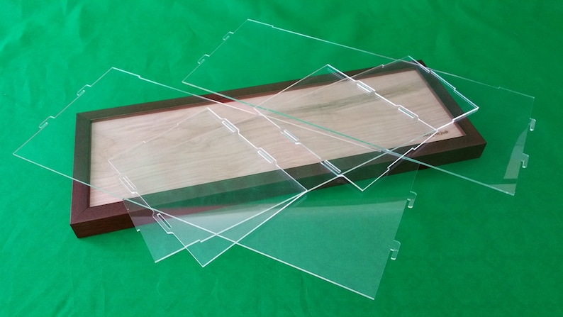 Op de afbeelding: Drie transparante acrylaatplaten met afgeronde hoeken en uitsparingen aan de randen, gestapeld op een houten frame met een lichtbruin houten oppervlak.