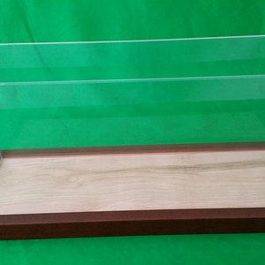May include: A clear acrylic display case with a wooden base. The case has a brown wooden base and a clear acrylic top. The case is empty.