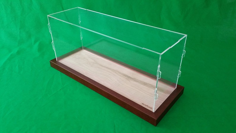 Op de afbeelding: Een transparante acryl display case met een houten basis. De basis is lichtbruin van kleur met een houtnerfpatroon. De case is rechthoekig en heeft een scharnierend deksel.